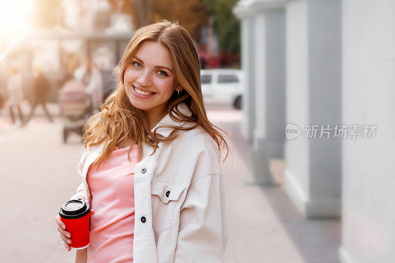 可爱的金发女孩走在城市的一杯咖啡和微笑