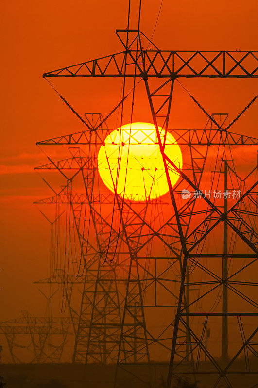 炎炎夏日，太阳落在一排高压输电塔后面