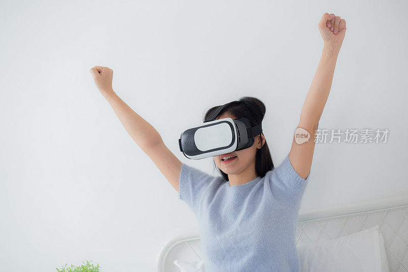 年轻的亚洲女性戴着vr头戴设备在家里兴奋地玩游戏，女性使用虚拟现实或元宇宙创新模拟3D，生活方式和技术概念。