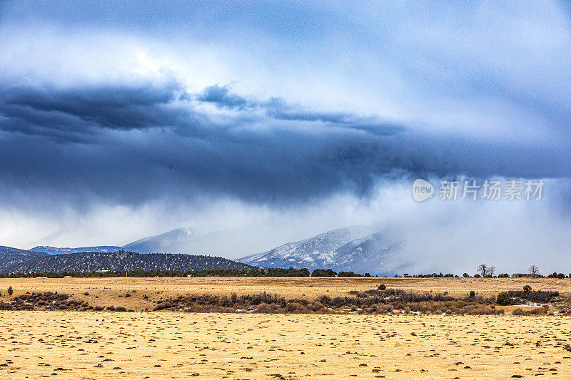 戏剧性的风暴云和雨在平坦的农田和雪山上移动