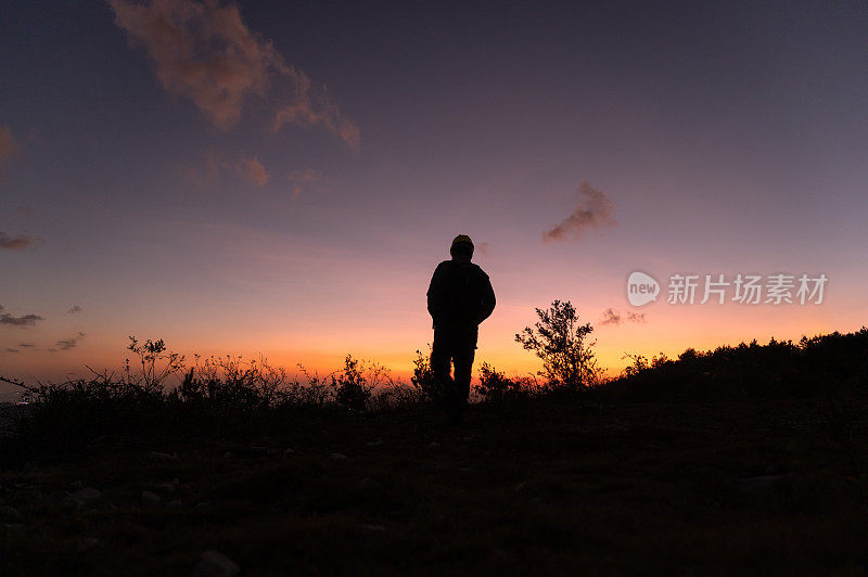 黄昏时一个人走在山顶上的剪影，面对着红色的天空和夕阳