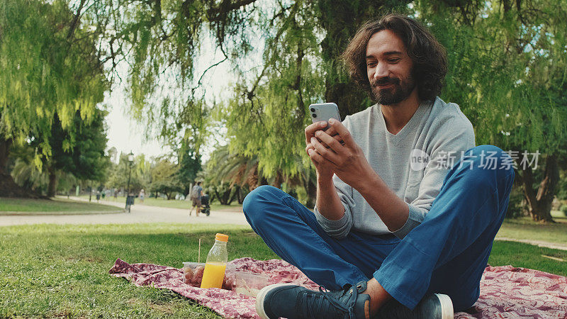 年轻男子坐在公园的草坪上使用手机