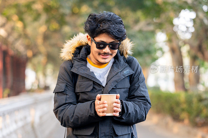 一个穿着冬季夹克，手里拿着咖啡杯的年轻人的肖像