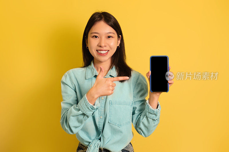 微笑的亚洲女人指着手机空屏幕，为你的网站做广告，提供广告空间，模型
