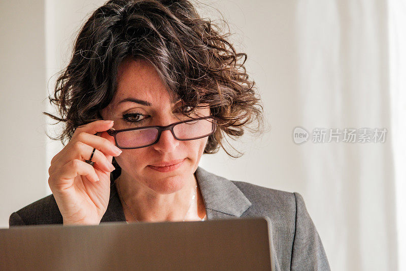 工作妇女看着笔记本电脑屏幕，拿着眼镜