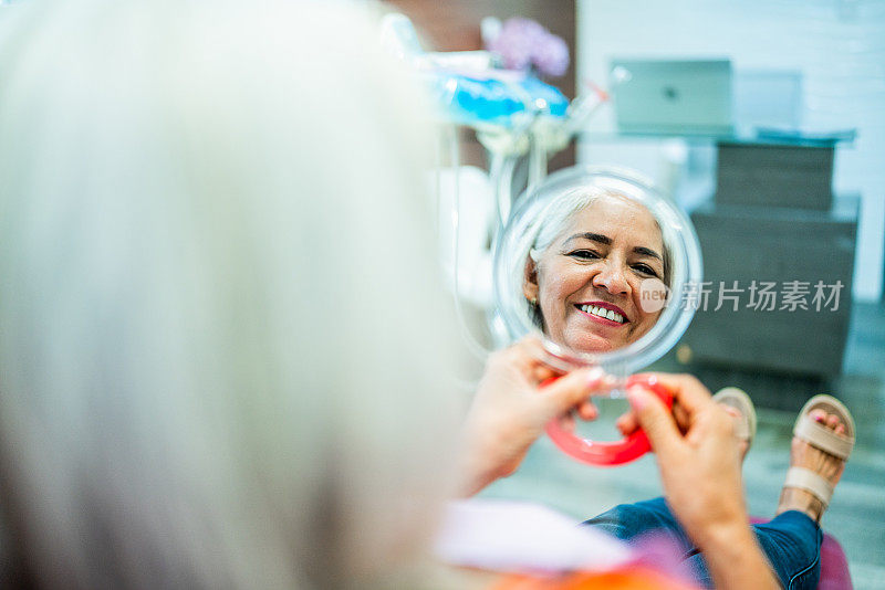一位老年妇女在牙医诊所的镜子前看着自己的牙齿