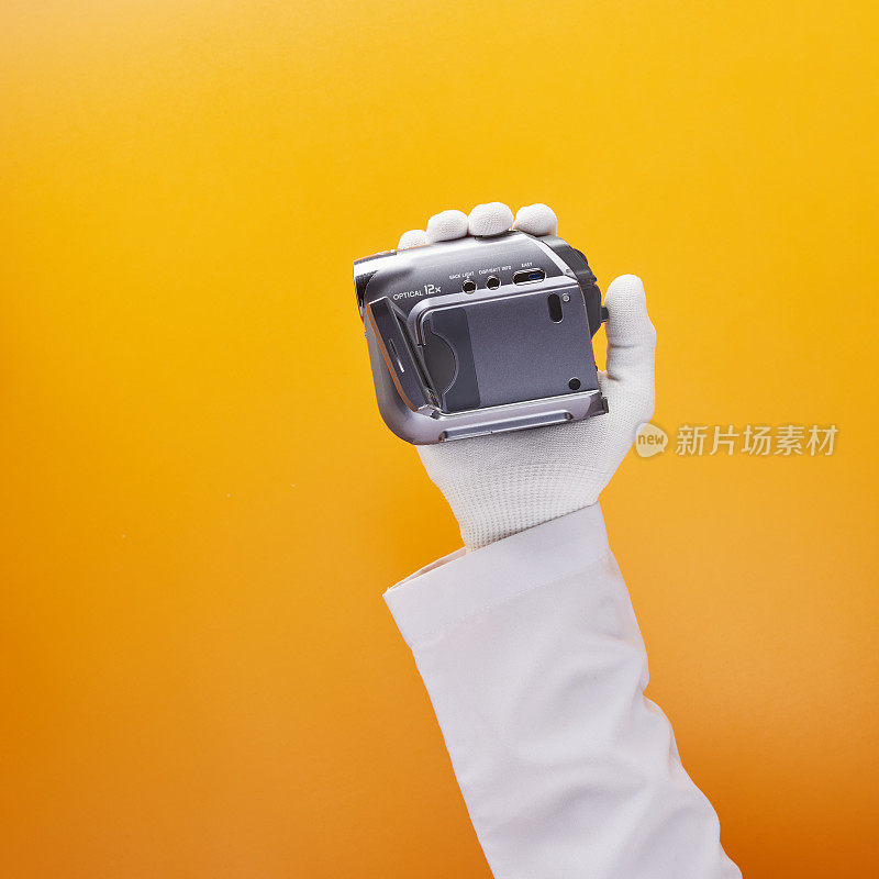 技术员戴着白手套，拿着黄橙色背景的迷你DV摄像机