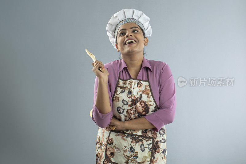 女厨师拿着勺子和抹刀站在白色的背景上