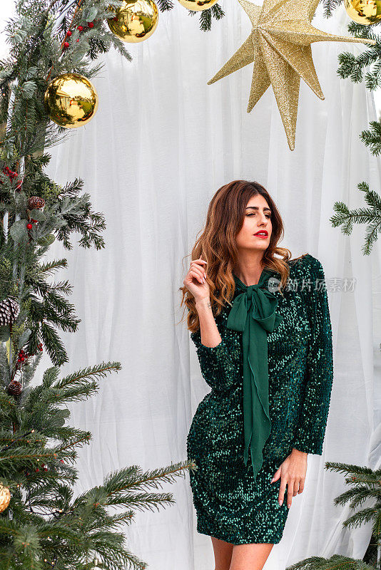 女人穿着优雅的绿色连衣裙在明亮的冬日圣诞树拱门场景中温暖的阳光