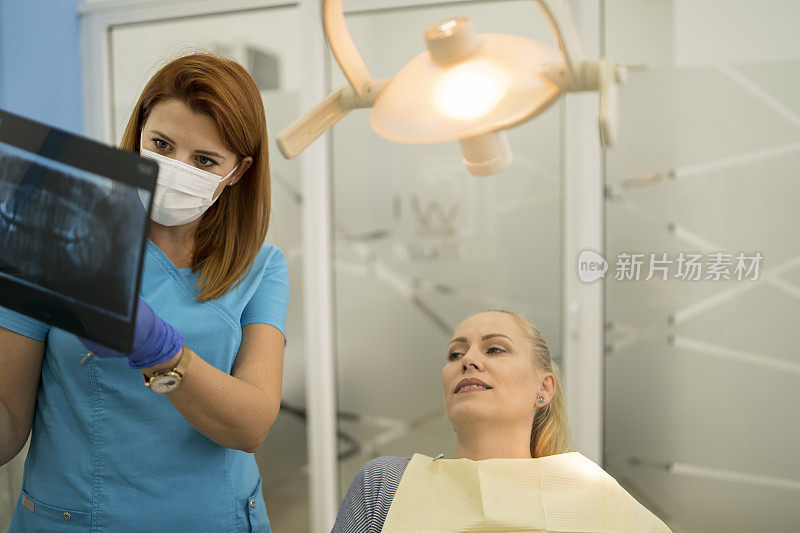 女牙医在牙科诊所与显示牙齿x光片的病人谈话