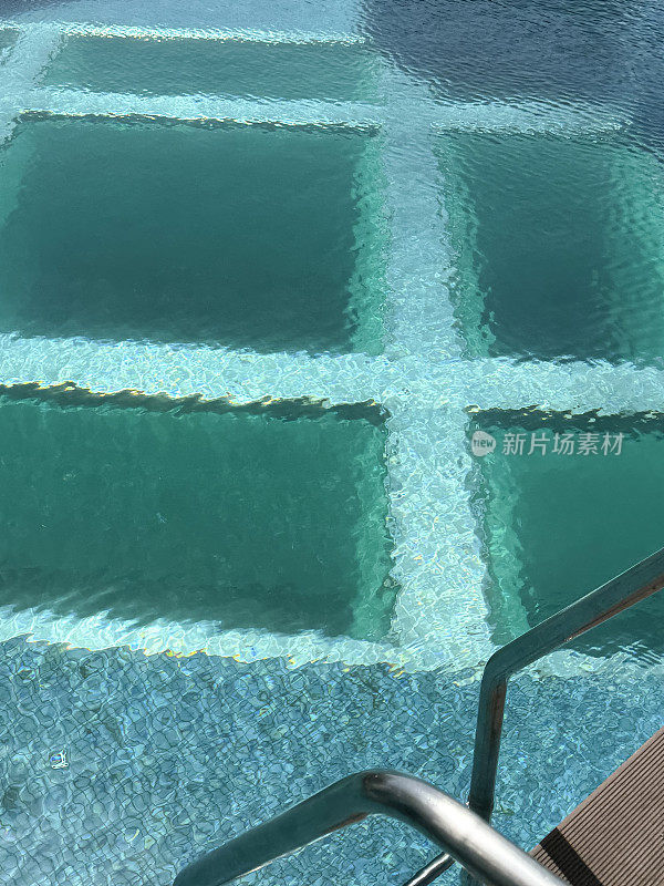 泳池底部有玻璃窗，泳池边有金属扶手的台阶通往水中，居高临下的景色