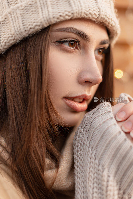 一个漂亮性感的女模特的特写肖像，棕色的眼睛，穿着时髦的外套，带着针织帽，夹克和复古毛衣在户外取暖。女性冬季风格与美容