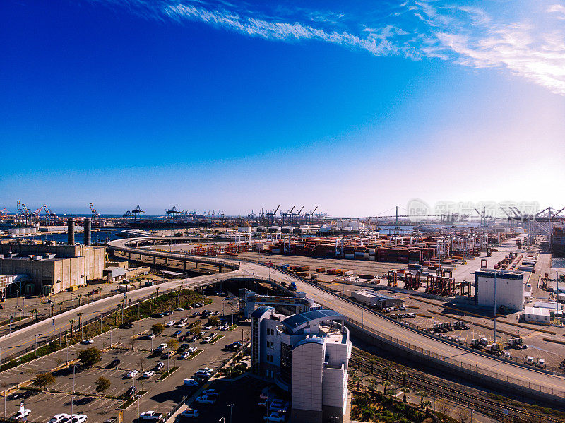 从上空俯瞰，洛杉矶港是一个熙熙攘攘的船坞，有高耸的起重机，一排排的集装箱和停靠的船只，形成了一个迷宫般的国际贸易和商业中心。