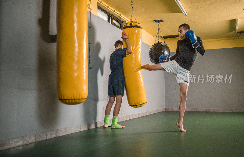 泰拳拳手在体育馆里通过踢他最好的朋友拿着的沙袋来训练