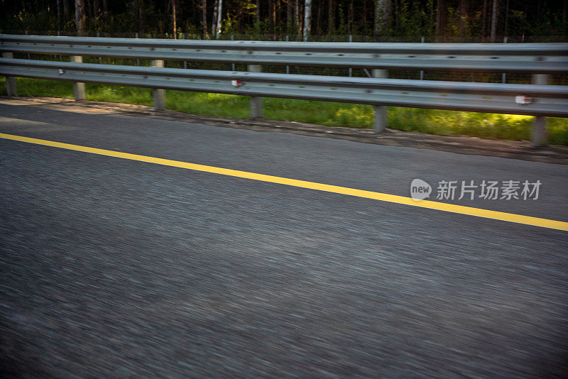 道路屏障、沥青路面与黄色分界线模糊在动，公路旅行概念