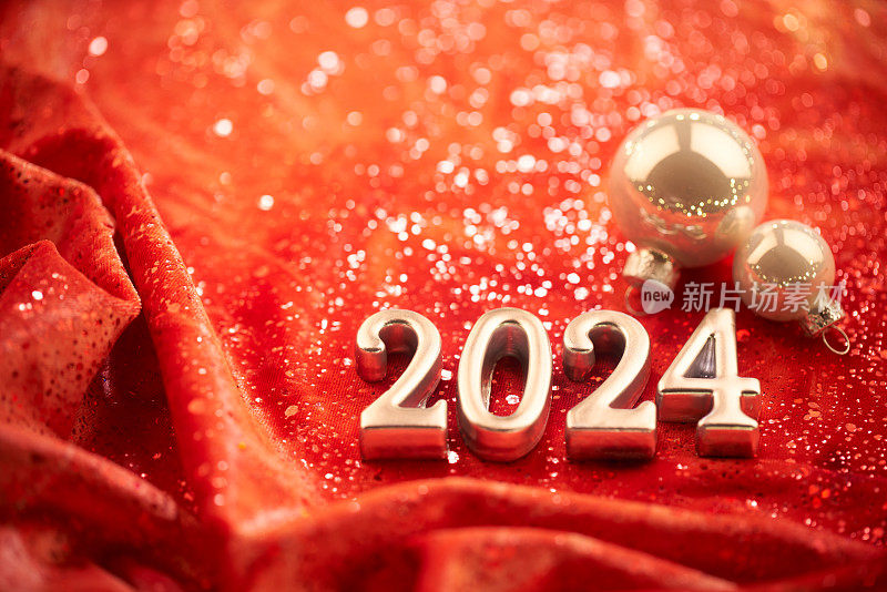 2024年新年快乐!闪亮的数字在红色的织物背景与圣诞装饰。