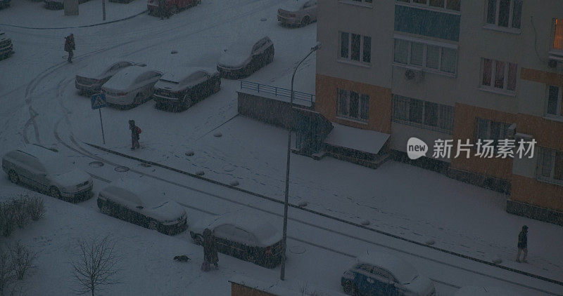 城市里冬天的早晨。住宅楼、摩天大楼。人们在雪中上班，天黑了。降雪，停着的汽车，俯视图。