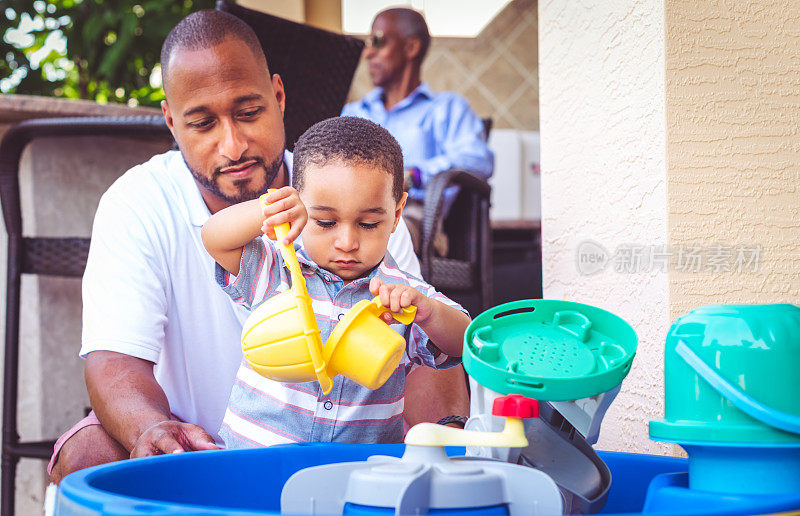 一位非裔美国父亲和他的小儿子在户外玩院子里的玩具