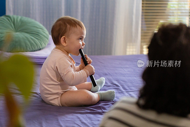 白人女婴坐在床上嚼电视遥控器