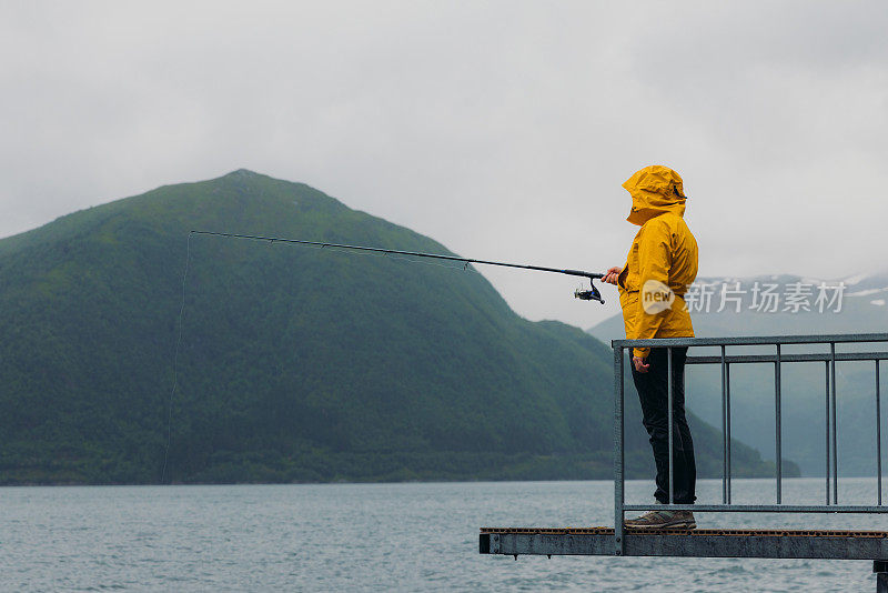 身穿黄夹克的男子在挪威峡湾边钓鱼