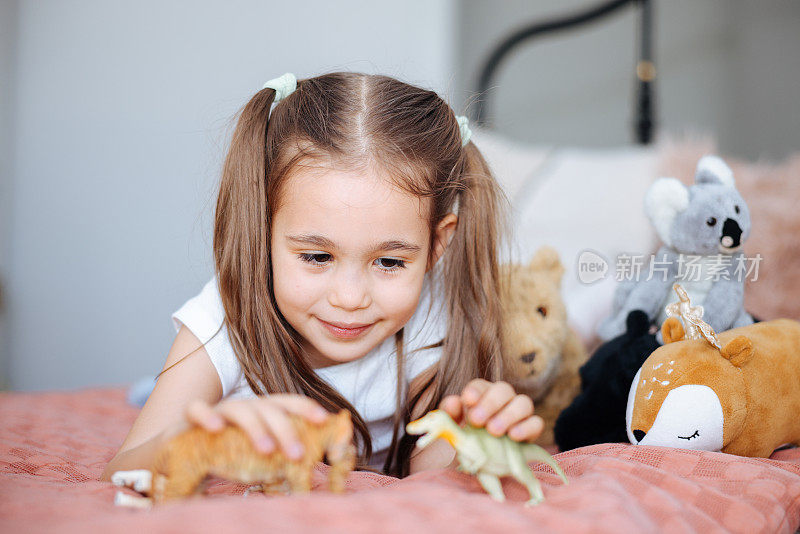 活泼可爱的孩子在卧室里玩塑料恐龙玩具。活泼可爱的孩子在卧室里玩塑料恐龙玩具。