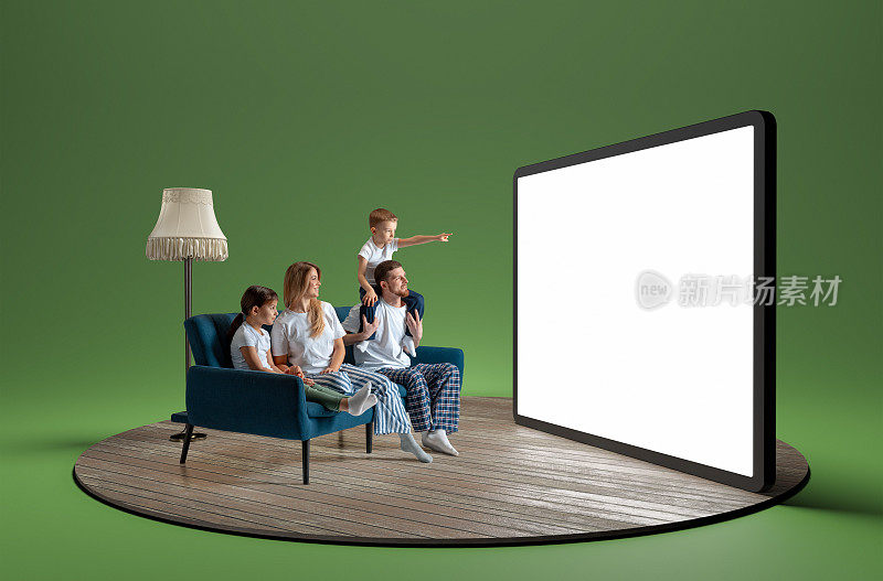 幸福的年轻家庭穿着睡衣，男人，女人和孩子坐在沙发上，看着巨大的3D模型平板电脑与空屏幕