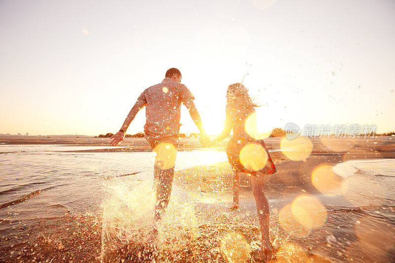 一对快乐的夫妇在阳光照耀的海滩上冲过海浪
