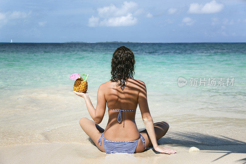 一个在热带海滩上喝着菠萝饮料的女人