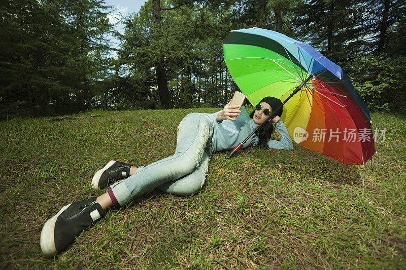 时尚女孩躺在五颜六色的雨伞下使用智能手机。