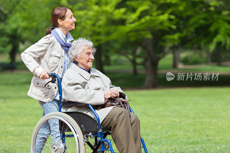 坐在轮椅上的老年妇女和家庭护工在公园里