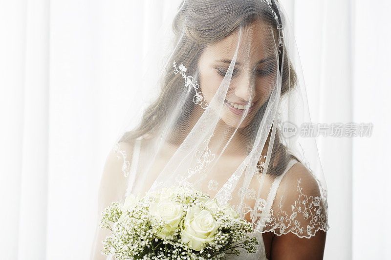 兴奋的年轻新娘戴着面纱捧着花束