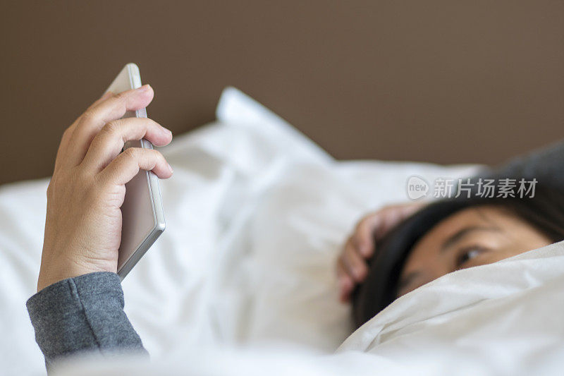 女孩躺在床上，看手机