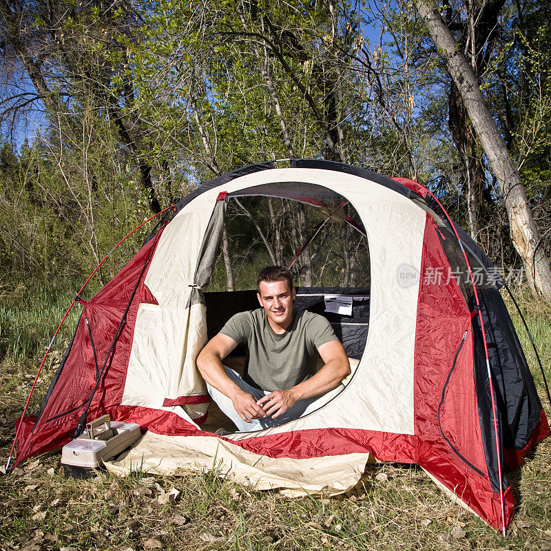 一名男子坐在红色帐篷里微笑着露营
