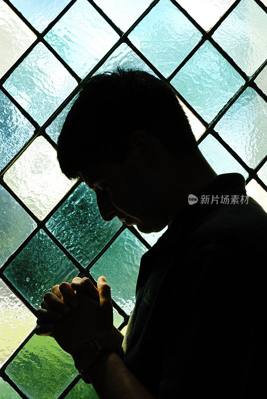 彩色玻璃窗前祈祷男孩的剪影