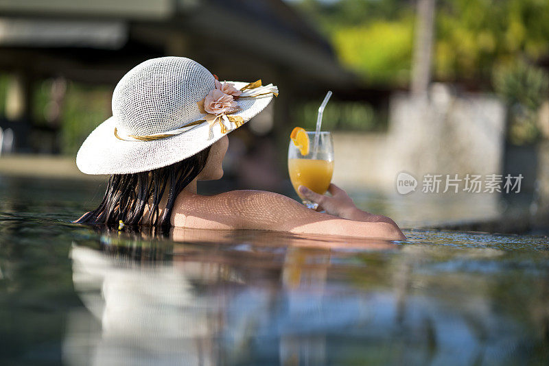 戴着太阳帽的女人在泳池里享受夏日鸡尾酒。