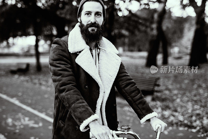 在秋天，大胡子的家伙穿着时髦的外套骑着一辆老式自行车。黑白照片