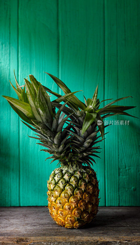新鲜的双头热带菠萝站在一张质朴的木桌上，背景是绿松石木墙。