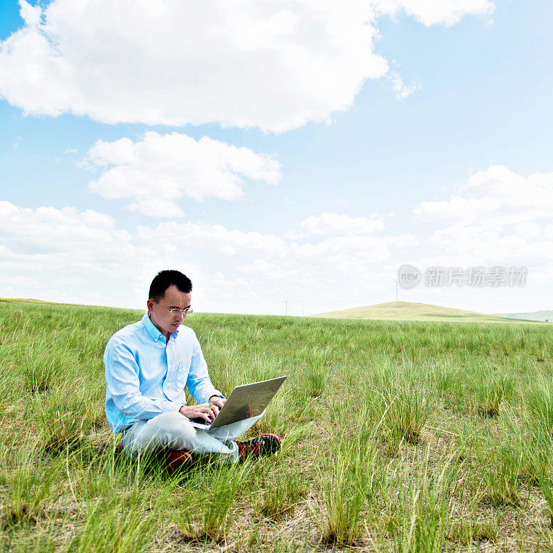 一个男人在草地上用笔记本电脑