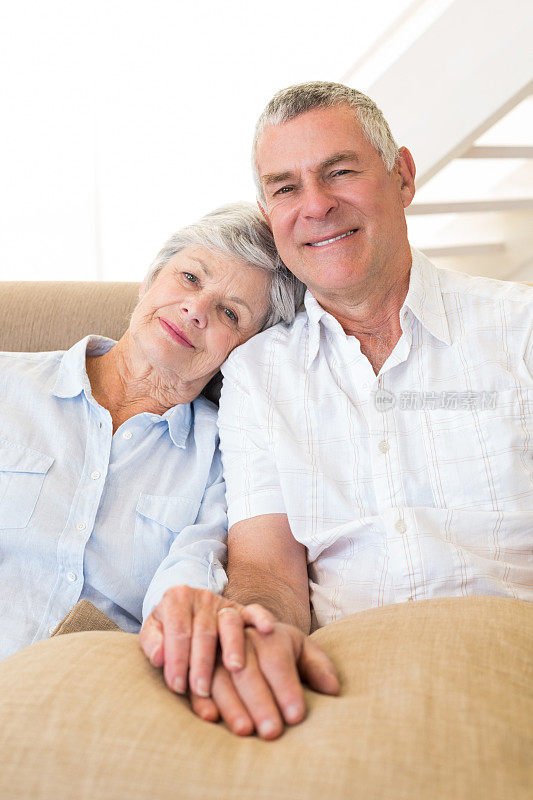 一对退休夫妇手牵着手坐在沙发上对着镜头微笑