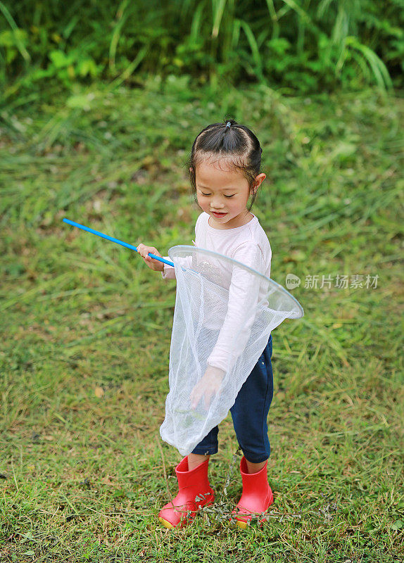 可爱的亚洲小女孩在田野与昆虫网在夏天。