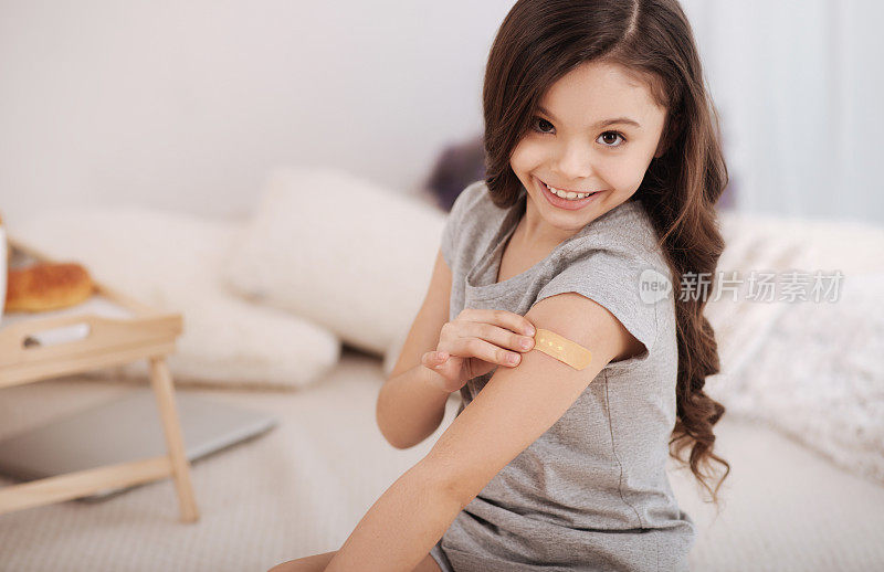 高兴的女孩在家里给手臂贴医用贴片