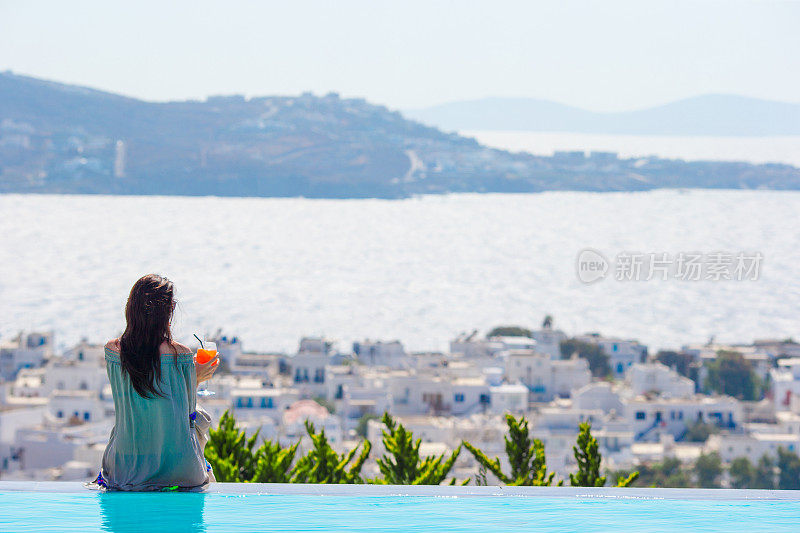 年轻女子放松在泳池边与惊人的希腊景色的背影