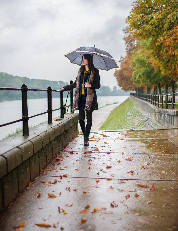 年轻女子撑着伞在秋雨中行走