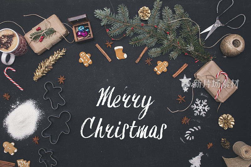 圣诞节的背景。俯视图女人的手写在粉笔牌子上。黑色的桌子上放着包装好的礼物和云杉树枝。准备手工新年装饰品的工作场所。