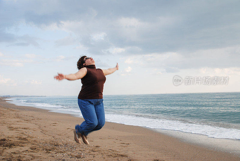 积极成熟的女人在海滩上跳冬天。