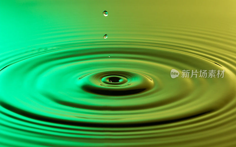 水滴近距离与同心涟漪在五颜六色的绿色和黄色的表面