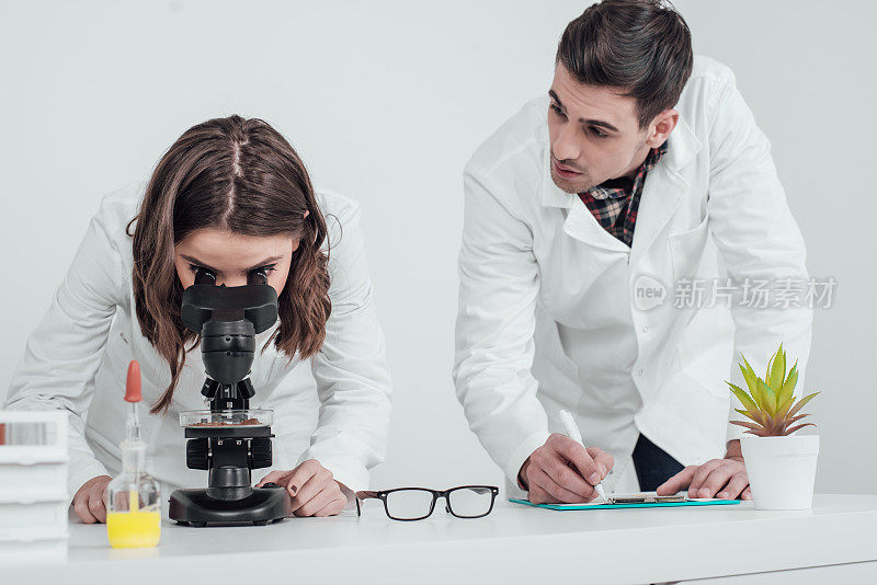 女科学家通过显微镜观察，男同事书写结果