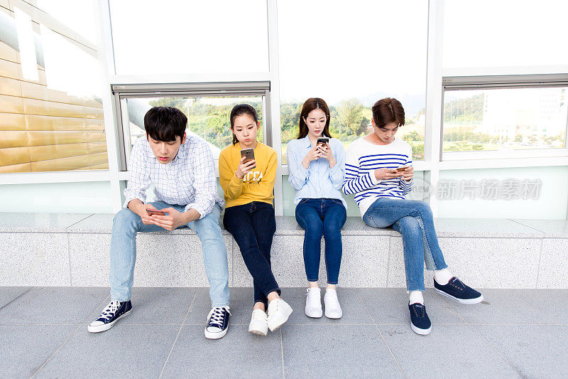 韩国人，大学生，坐着(身体姿势)，智能手机，面无表情，走廊(建筑的一部分)