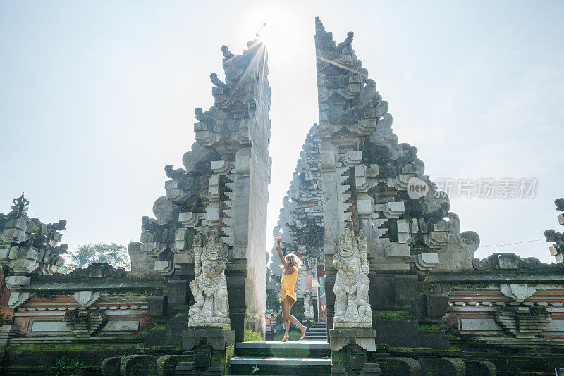 女人旋转跳舞像快乐的女孩在寺庙的入口门前在乌布，巴厘岛-人们旅游目的地乐趣的生活方式概念