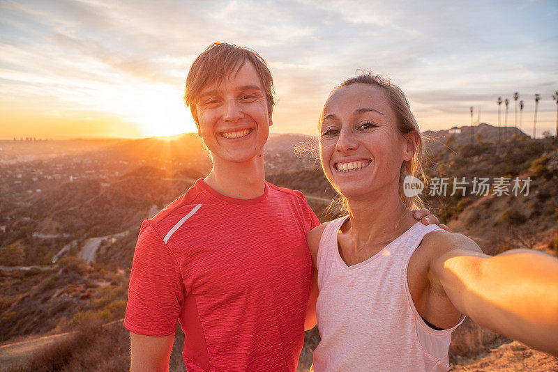 一对运动的年轻夫妇在日落时分在城市上方自拍